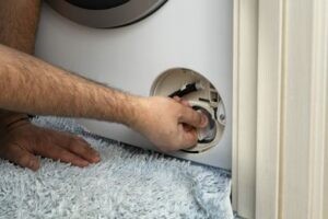 Мастер по ремонту стиральных машин откручивает крышку сливного фильтра