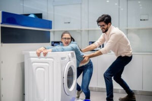 Муж и жена пытаются передвинуть тяжелую стиральную машину вдвоем